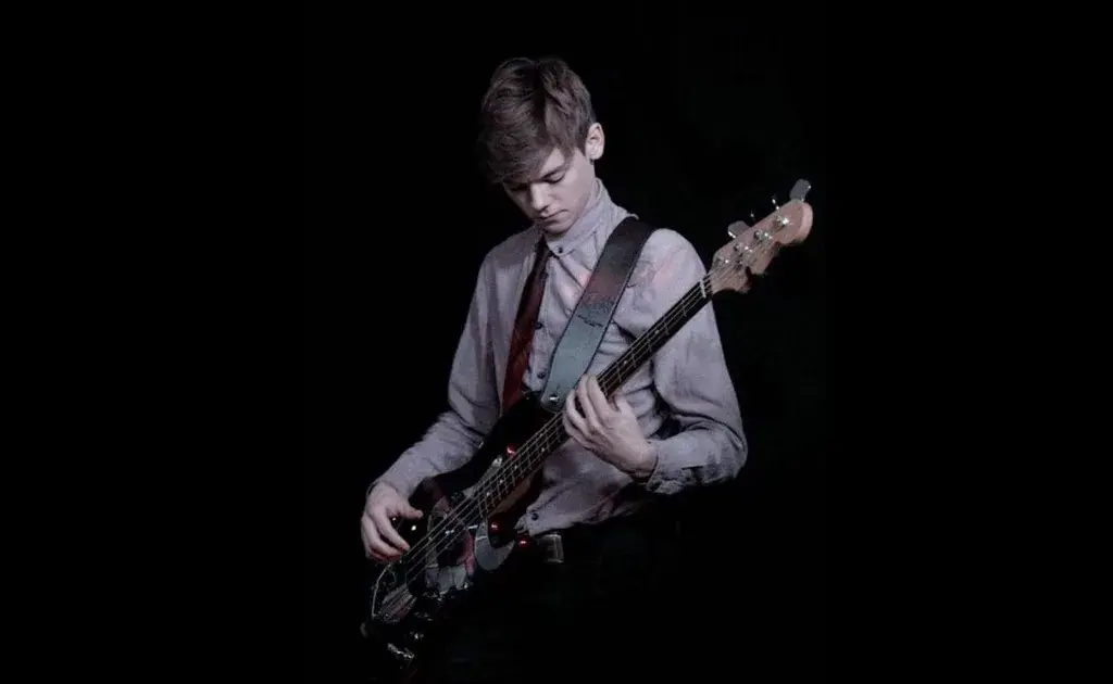 Thomas Brodie-Sangster tocando baixo demonstrando seu talento musical além da carreira como ator
